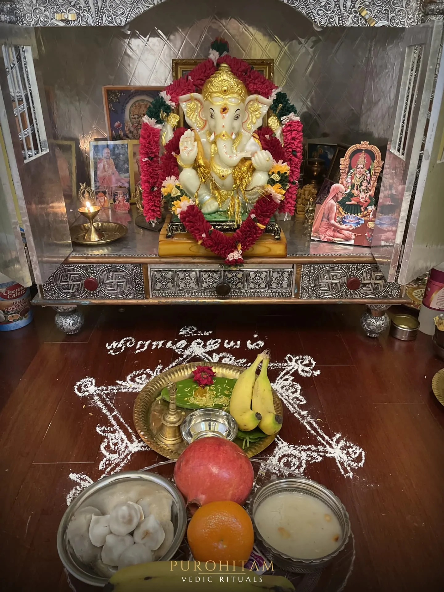 Flower garlanded Lord Ganesha shrine with traditional offerings and kolam