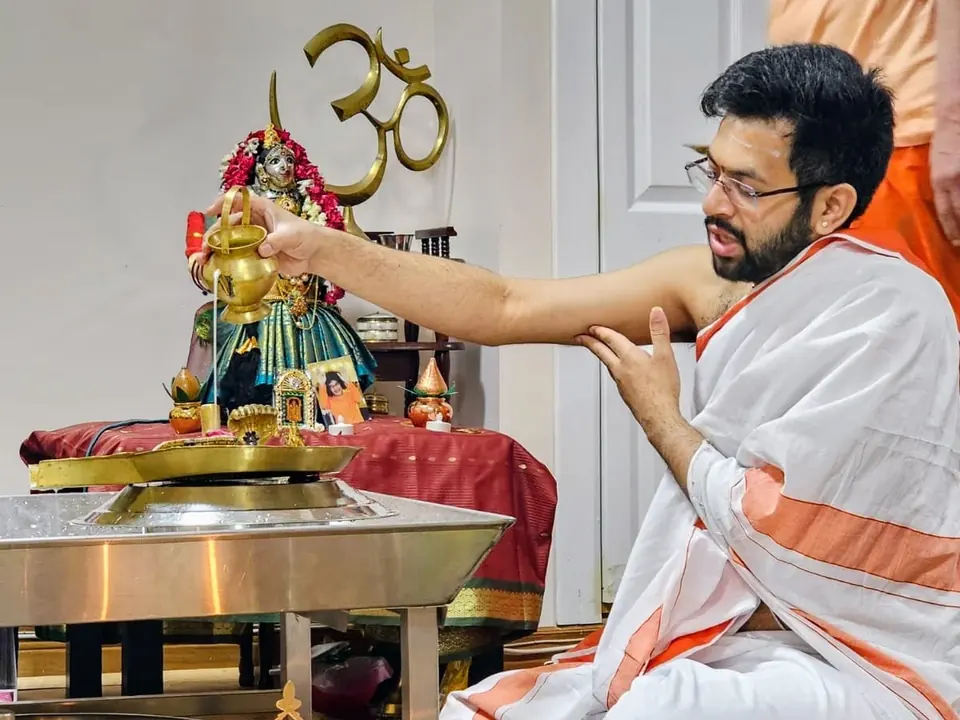 Purohit seated on the floor performing ritual water offerings at a home altar
